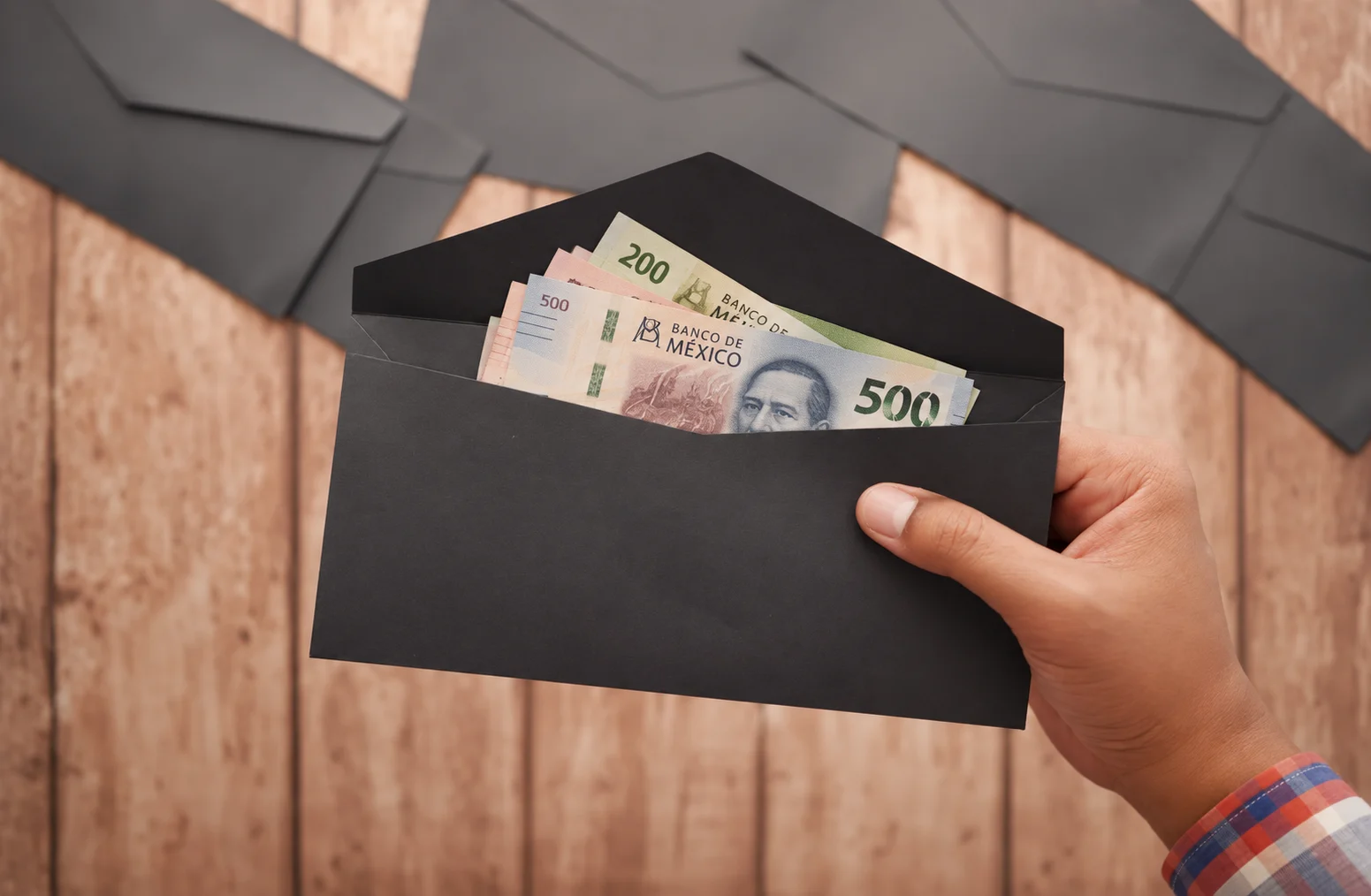 Una mano sosteniendo un sobre negro con billetes de pesos mexicanos
