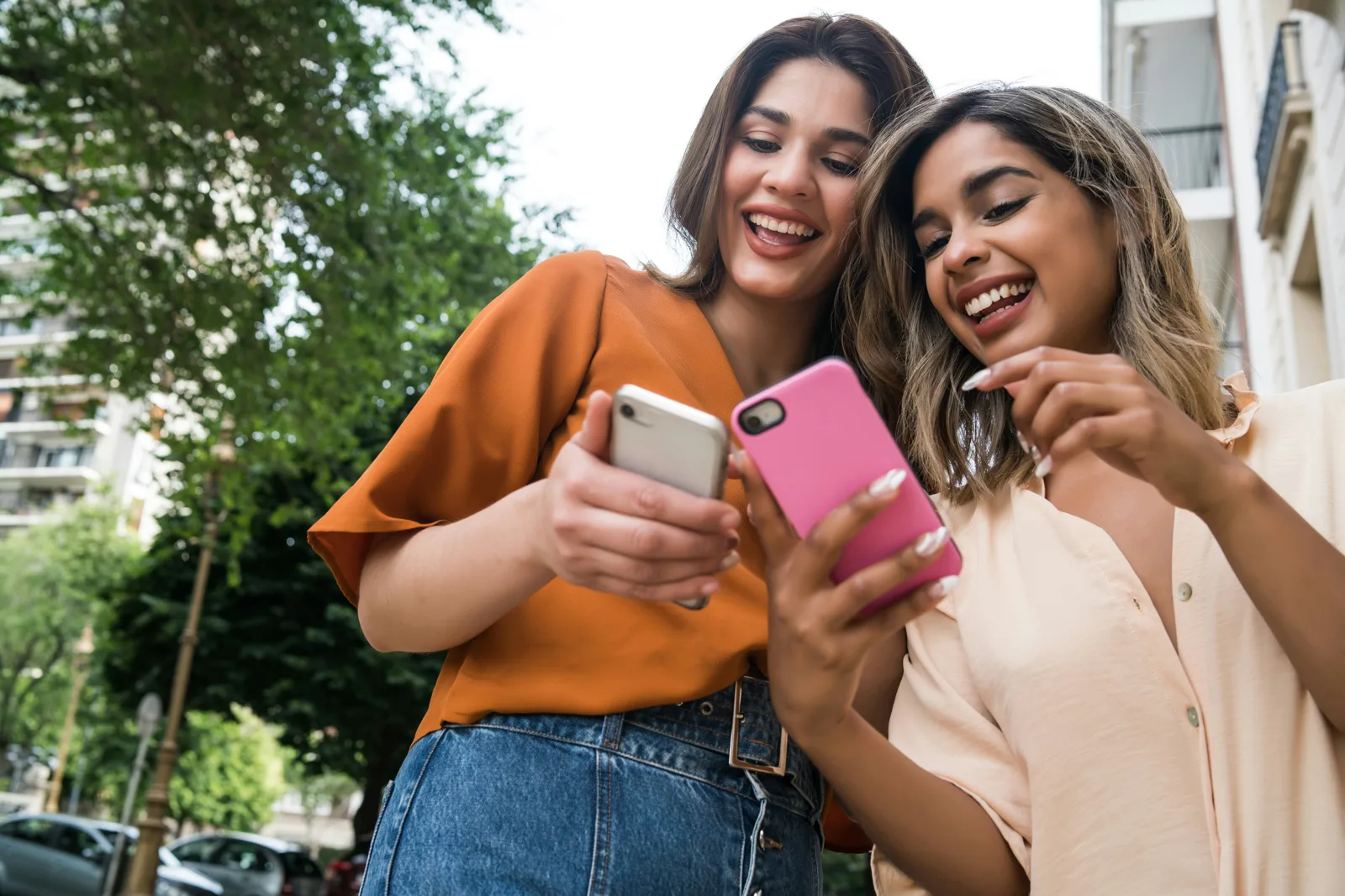 Dos amigas riendo mientras miran sus teléfonos